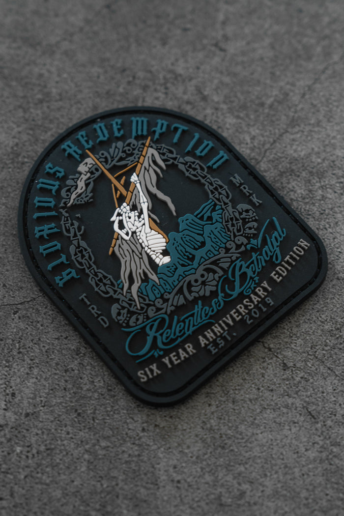 The Glorious Redemption Patch by Relentless Betrayal features a hooded figure climbing a rocky mountain on gray PVC, with chain designs and text: Relentless Betrayal, Six Year Anniversary Edition, 5-5-2019.