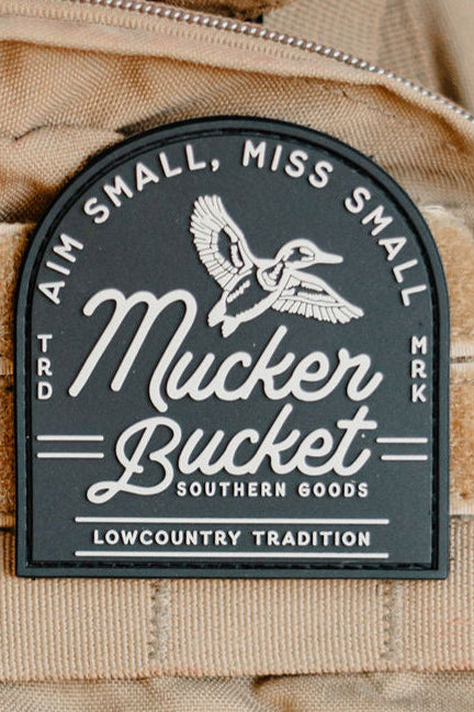 Mucker Bucket patch on a beige background