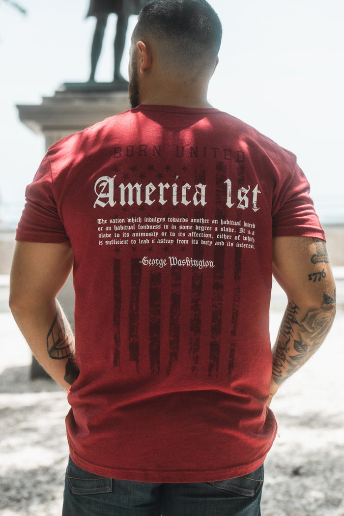 Person wearing a red t-shirt with text on the back, standing outdoors with a statue and palm tree in the background.