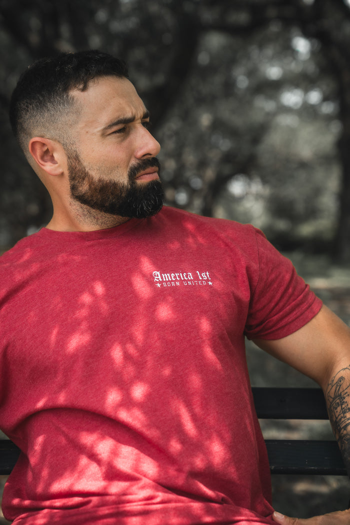 Man wearing a red t-shirt with text, sitting outdoors with trees in the background