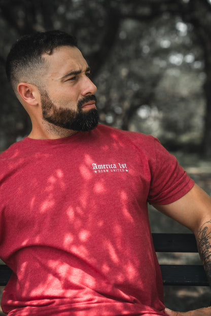Man wearing a red t-shirt with text, sitting outdoors with trees in the background