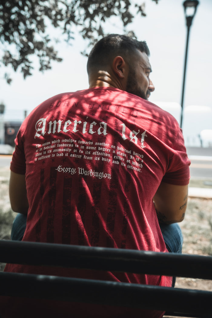 Man wearing a red t-shirt with text on the back, sitting outdoors.