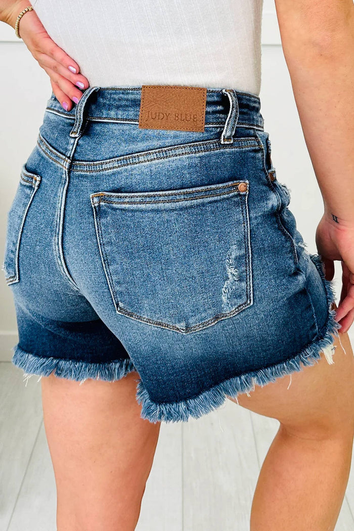 Blue denim shorts with frayed hem worn by a person on a light background