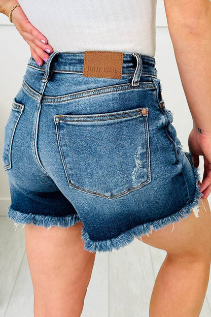 Blue denim shorts with frayed hem worn by a person on a light background