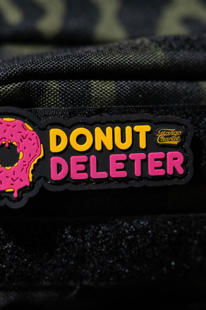 The Donut Deleter - Patch by Tango Charlie Apparel is a 3-inch 3D PVC patch with a pink sprinkled donut and “DONUT DELETER” in yellow/pink, plus a small Giant Mouse logo. It attaches to fabric surfaces with Velcro backing.