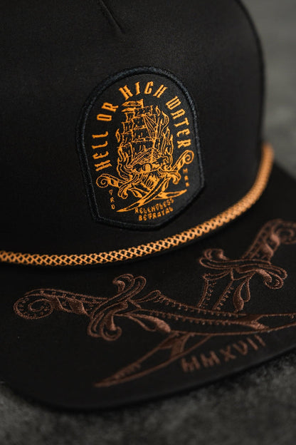 The Relentless Betrayal Hell Or High Water Snapback is water-resistant with a black base, an orange ship patch, and Hell or High Water. It features swords on the brim, MMXVII in brown, and a gold chain—ideal for expressing resilience and style.