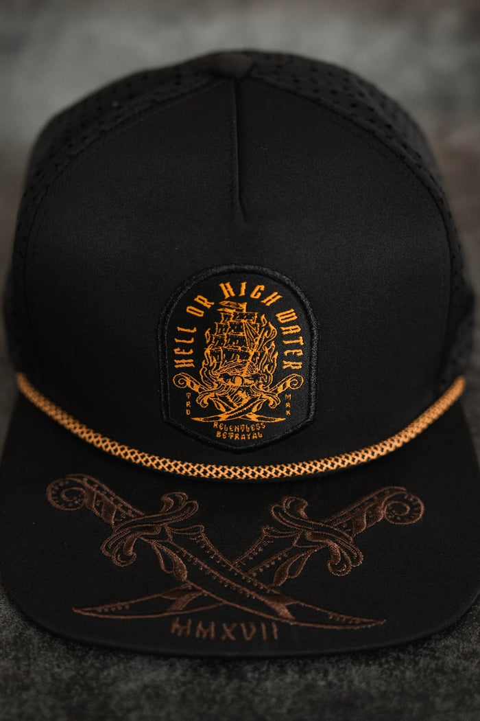 The Hell Or High Water Snapback by Relentless Betrayal is a black cap featuring a golden embroidered ship patch with Hell or High Water and Relentless Serenity. Its brim has crossed swords, and the year MMXVII shines in gold, representing resilience.