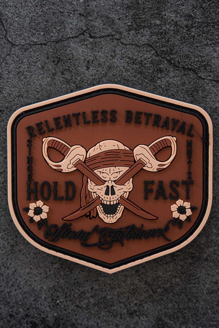 The Hold Fast Patch by Relentless Betrayal is a 3-inch Velcro patch featuring a skull with a bandana and crossed swords, surrounded by "Relentless Betrayal, Hold Fast," floral accents, and set on a dark textured background.
