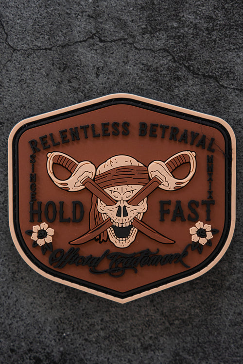 The Hold Fast Patch by Relentless Betrayal is a 3-inch Velcro patch featuring a skull with a bandana and crossed swords, surrounded by "Relentless Betrayal, Hold Fast," floral accents, and set on a dark textured background.