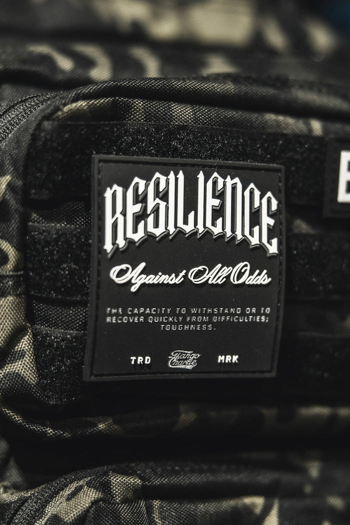 A close-up of the Tango Charlie Apparel "Resilience - Patch," a 3D PVC patch on a camo bag, featuring the phrase "RESILIENCE Against All Odds" to symbolize toughness and overcoming challenges.