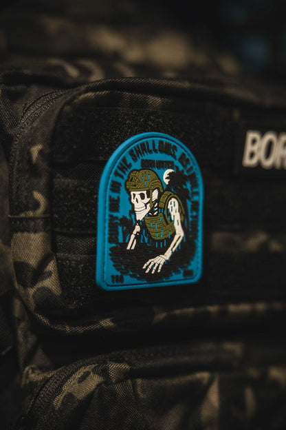 The Shallows PVC Patch by Born United Private Label features a skeleton in military gear rising from water on a blue and black camo background, with DOWN IN THE SHALLOWS REAP THE DEEP around the edge.